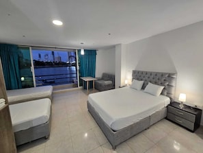 A modern hotel room with a large bed, a sofa, a small table, and a view of a cityscape through a sliding door. - MARINA DEL REY  (Cartagena)