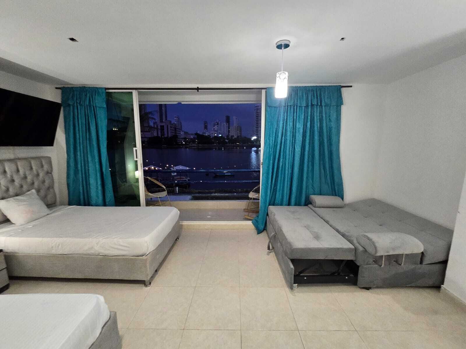 A hotel room with a bed, a sofa, and a view of a cityscape at night.