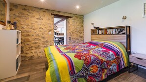 Une chambre avec un mur en pierre, une couvre-lit aux couleurs vives, une bibliothèque et un bureau.