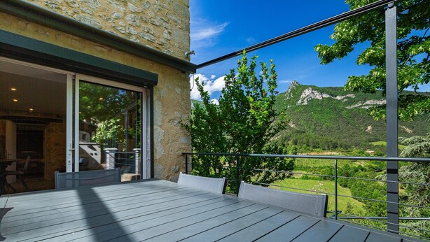 Un balcon donnant sur un paysage montagneux, un mur en pierre et une porte vitrée menant à un espace intérieur.