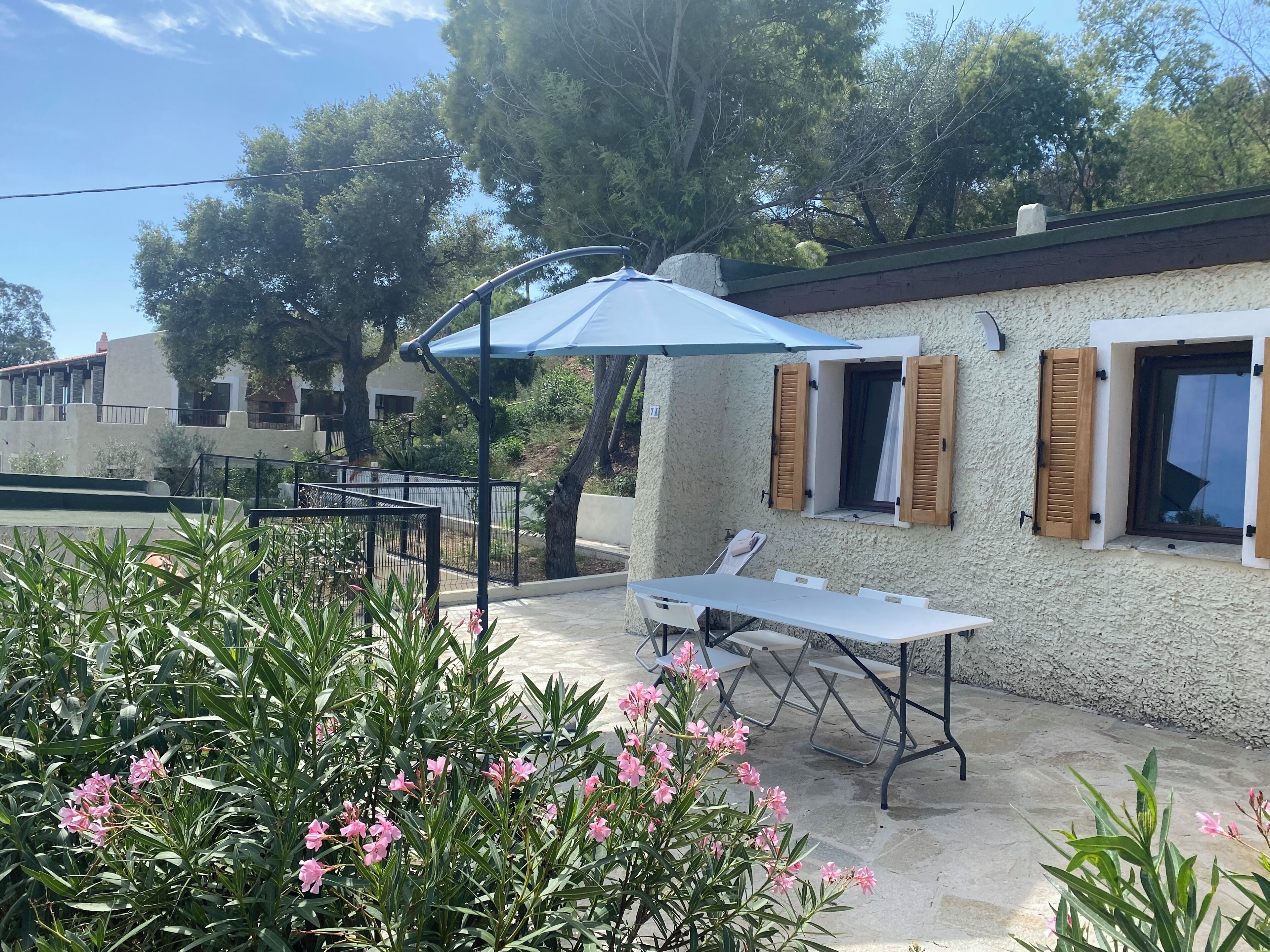 Un espace patio avec une table et des chaises, un parasol bleu et un mur blanc agrémenté de volets en bois.