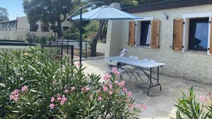 Un espace patio avec une table et des chaises, un parasol bleu et un mur blanc agrémenté de volets en bois.