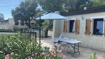 Un espace patio avec une table et des chaises, un parasol bleu et un mur blanc agrémenté de volets en bois.