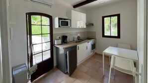 Une cuisine compacte équipée d’un four à micro-ondes, d’un grille-pain, d’une machine à café et d’un petit réfrigérateur. Une fenêtre laisse entrer la lumière naturelle et offre une vue sur la verdure environnante.