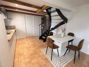 A modern kitchen with a built-in oven, a dining area with a white table and brown chairs, and a black spiral staircase leading to a loft bedroom. - Ty Glaz, on the road to the beaches... (Plobannalec-Lesconil)