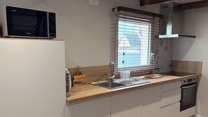 Una cocina moderna con microondas integrado, un lavabo con escurreplatos y una ventana con persianas.