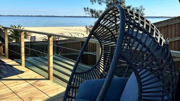 A wooden deck with a hanging chair overlooking a beach.