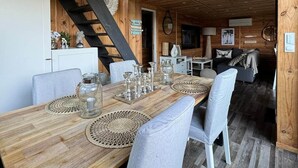 A wooden dining table with woven placemats, grey upholstered chairs, and a black spiral staircase leading to an upper level.