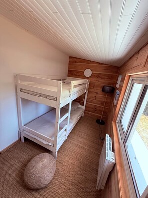 A bunk bed room with a wooden wall, a round mirror, and a window.