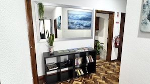 A hallway with a herringbone wooden floor, a black console table with books and a plant, and a large framed picture of the ocean. - Ocean View Guest House (Sao Vicente)