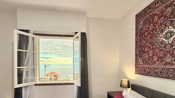 A hotel room with a bed, a view of the outside, a nightstand, and a wall tapestry. - Ocean View Guest House (Sao Vicente)