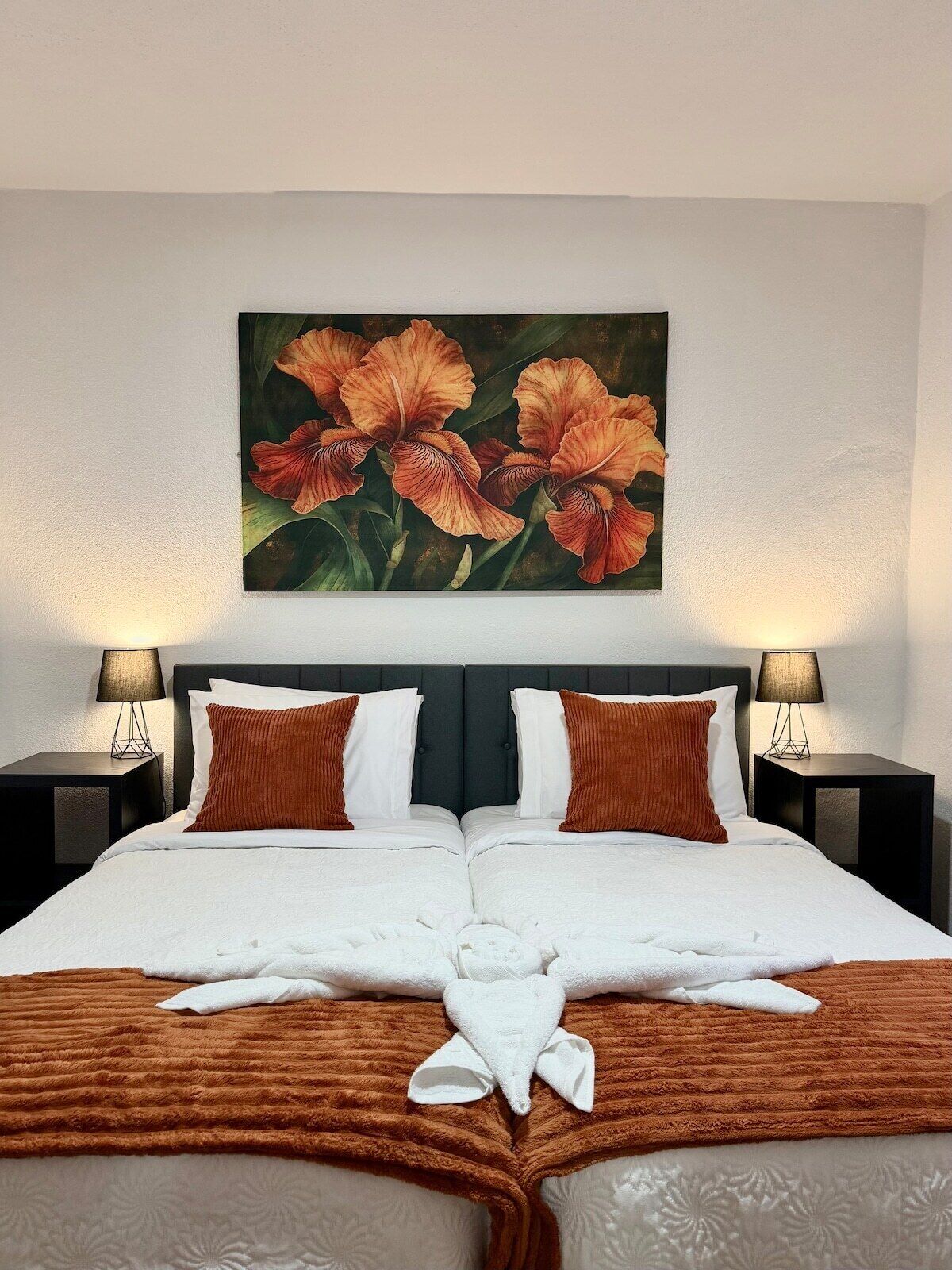 A hotel room with a large bed, two bedside tables with lamps, and a painting of flowers on the wall.