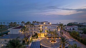 Ein modernes Hotel mit mehreren Etagen, einem zentralen Innenhof mit Palmen und Blick auf das Meer.
