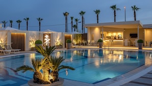 Ein Poolbereich mit Palmen, Liegestühlen und einer Bar.