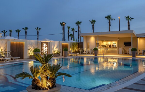 Ein Poolbereich mit Palmen, Liegestühlen und einer Bar.