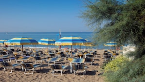 Una spiaggia con file di lettini e ombrelloni gialli e azzurri.