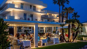 Ein mehrstöckiges Hotel mit Außenrestaurants, Palmen und einer überdachten Terrasse.