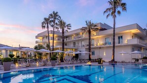 Ett modernt hotell med pool, palmer och solstolar.