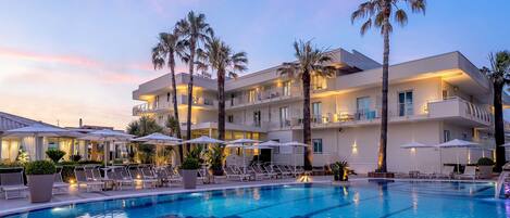 A modern hotel with a pool, palm trees, and lounge chairs.