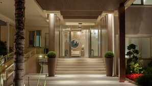 Una entrada imponente con una escalera que conduce a un área de recepción, con un diseño moderno que incluye una palmera y plantas en macetas.