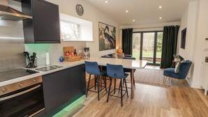 Una cocina moderna con horno integrado, un comedor con sillas azules y un ventanal con cortinas.