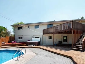 Una casa de dos pisos con piscina en el patio trasero, terraza de madera y un área exterior cubierta con escaleras.