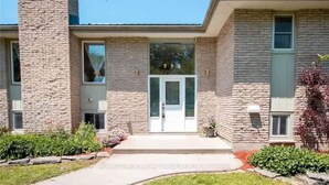 A two-story building with a stone facade, a central entrance with a glass door, and a small porch area. - Large Whole Home in Wine Country: Pool Hottub Sauna + Spacious Backyard & Nature (Prince Edward)