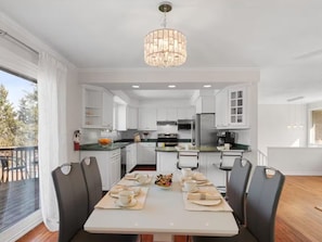 Una cocina moderna con armarios blancos, una mesa de comedor preparada para cuatro personas y una araña.