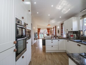 A modern kitchen with white cabinetry, a built-in oven, and a granite countertop. - Hazel Lodge (Craven Arms)