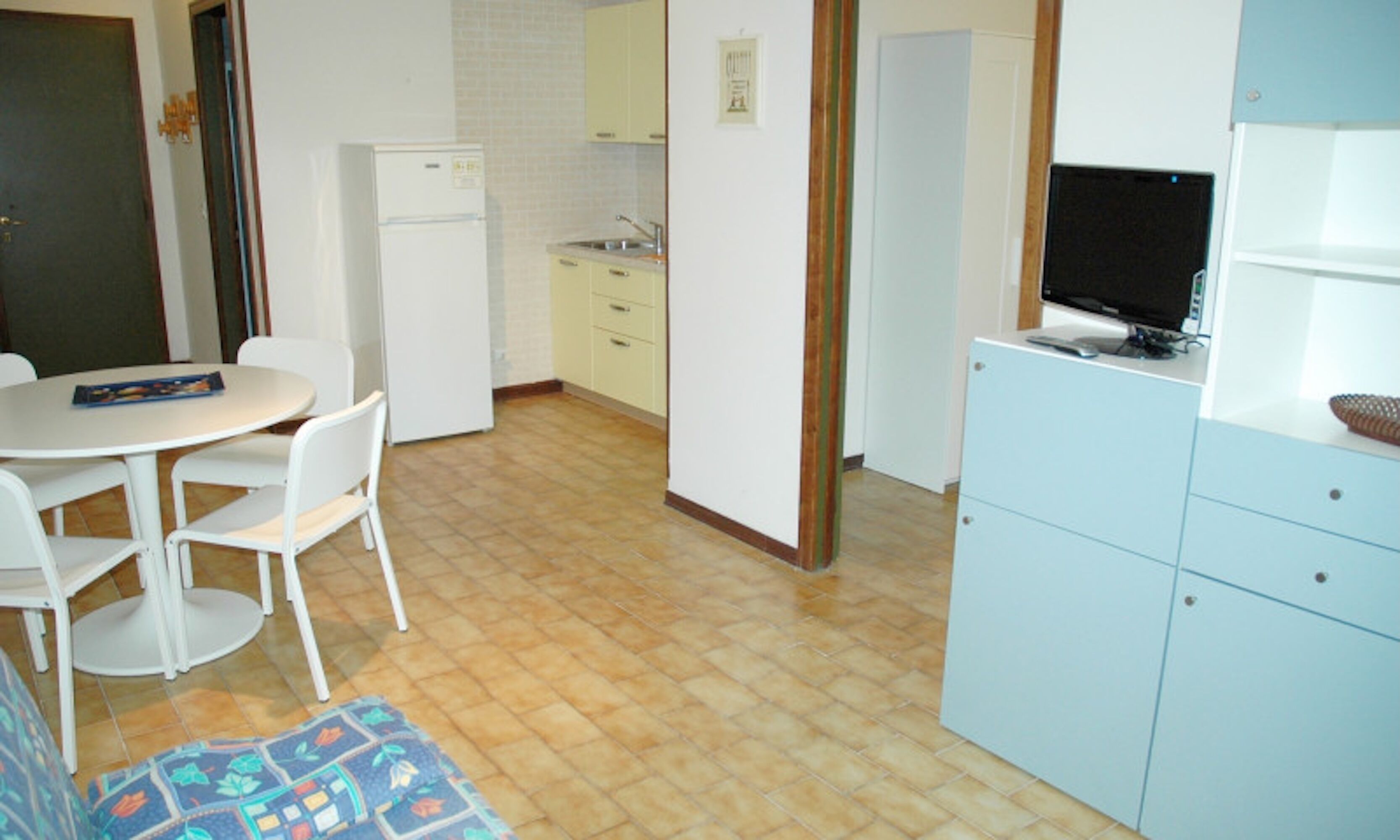 A compact kitchen with a refrigerator, sink, and a dining area with chairs.