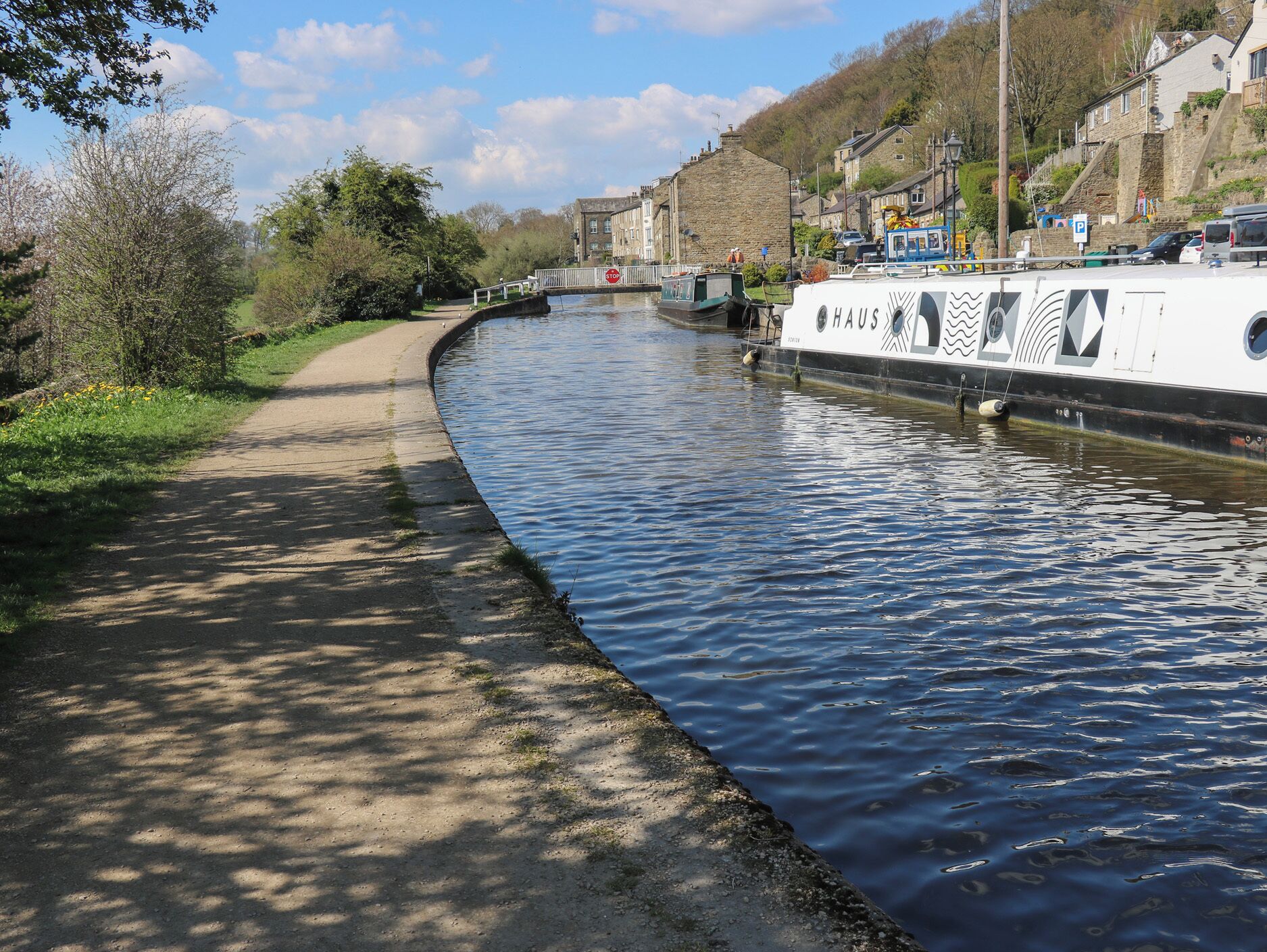 Ein schmaler Kanal mit einem am rechten Ufer vertäuten Boot, einem Fußweg links und Gebäuden im Hintergrund.