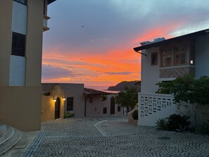 A cobblestone street leading to a building with a balcony, under a sunset sky. - Oceanview, beach club, plunge pool, steps to beach – Casa Olas (Las Catalinas)