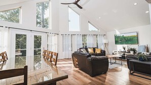 A spacious living room with a large glass dining table, leather sofas, and a ceiling fan. - Lakefront Home w/Private Dock, Hot Tub (LaFollette)