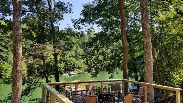 A wooden deck with outdoor seating and a view of a lake surrounded by trees. - Lakefront Home w/Private Dock, Hot Tub (LaFollette)
