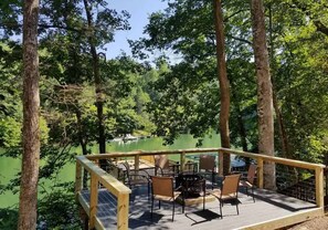 Um deck de madeira com área de estar ao ar livre e vista para um lago rodeado por árvores.