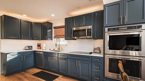 A modern kitchen with dark blue cabinets, stainless steel appliances, and a wooden floor. - Lakefront Home w/Private Dock, Hot Tub (LaFollette)