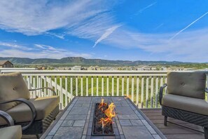 Eine Terrasse mit Feuerstelle, zwei Stühlen und Blick auf eine Wohngegend mit Häusern und Bergen im Hintergrund.