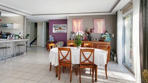 A dining area with a round table, chairs, and a kitchen in the background. - Bed and Breakfast 'Les Boubous-Nono' with Shared Terrace, Shared Garden and Wi-Fi (Saint-Nazaire)