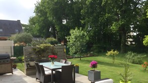 An outdoor patio with a table and chairs, a grill, and a garden with various plants and flowers. - Bed and Breakfast 'Les Boubous-Nono' with Shared Terrace, Shared Garden and Wi-Fi (Saint-Nazaire)