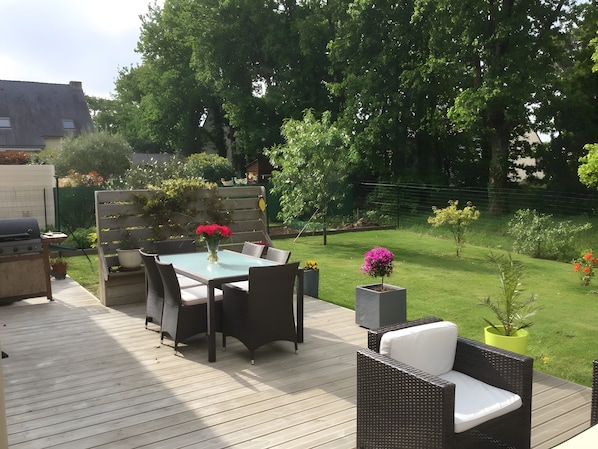 An outdoor patio with a table and chairs, a grill, and a garden with various plants and flowers.