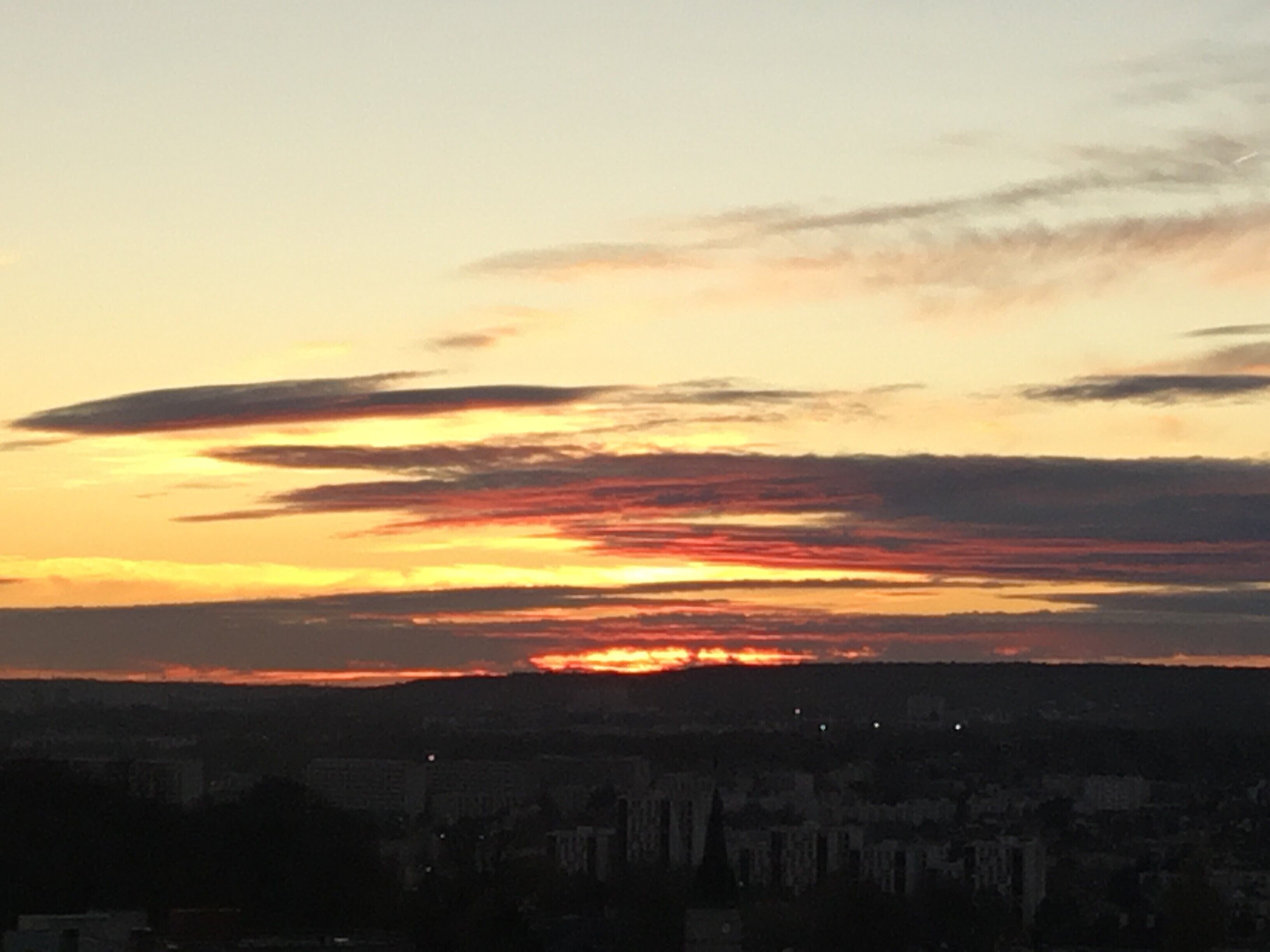 Un coucher de soleil sur une ville, avec des bâtiments bien visibles et un ciel dégagé.