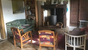 Un saló acollidor amb una llar de foc, un sofà verd escocès, una cadira de fusta i una catifa estampada.