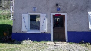 Un edifici de dos pisos amb teulada de rajola, una finestra petita i una porta amb cortina vermella.