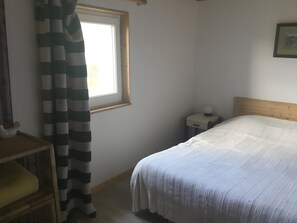 A bedroom with a bed, a nightstand, a window, and a curtain.