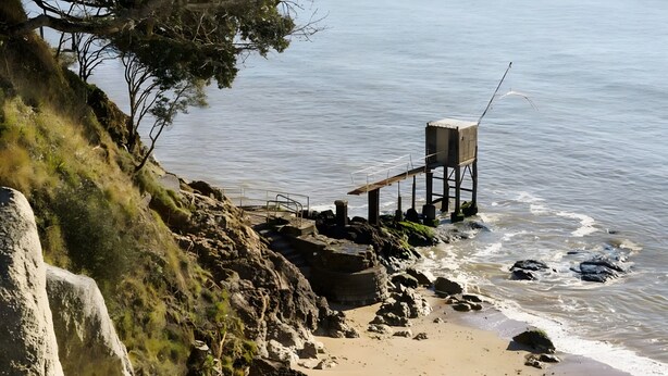 Una playa costera con terreno rocoso, una estructura de madera y una vista despejada del mar.