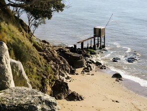 A coastal beach with rocky terrain, a wooden structure, and a clear view of the sea.