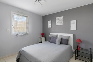 A bedroom with a bed, a nightstand, a red lamp, and wall art.