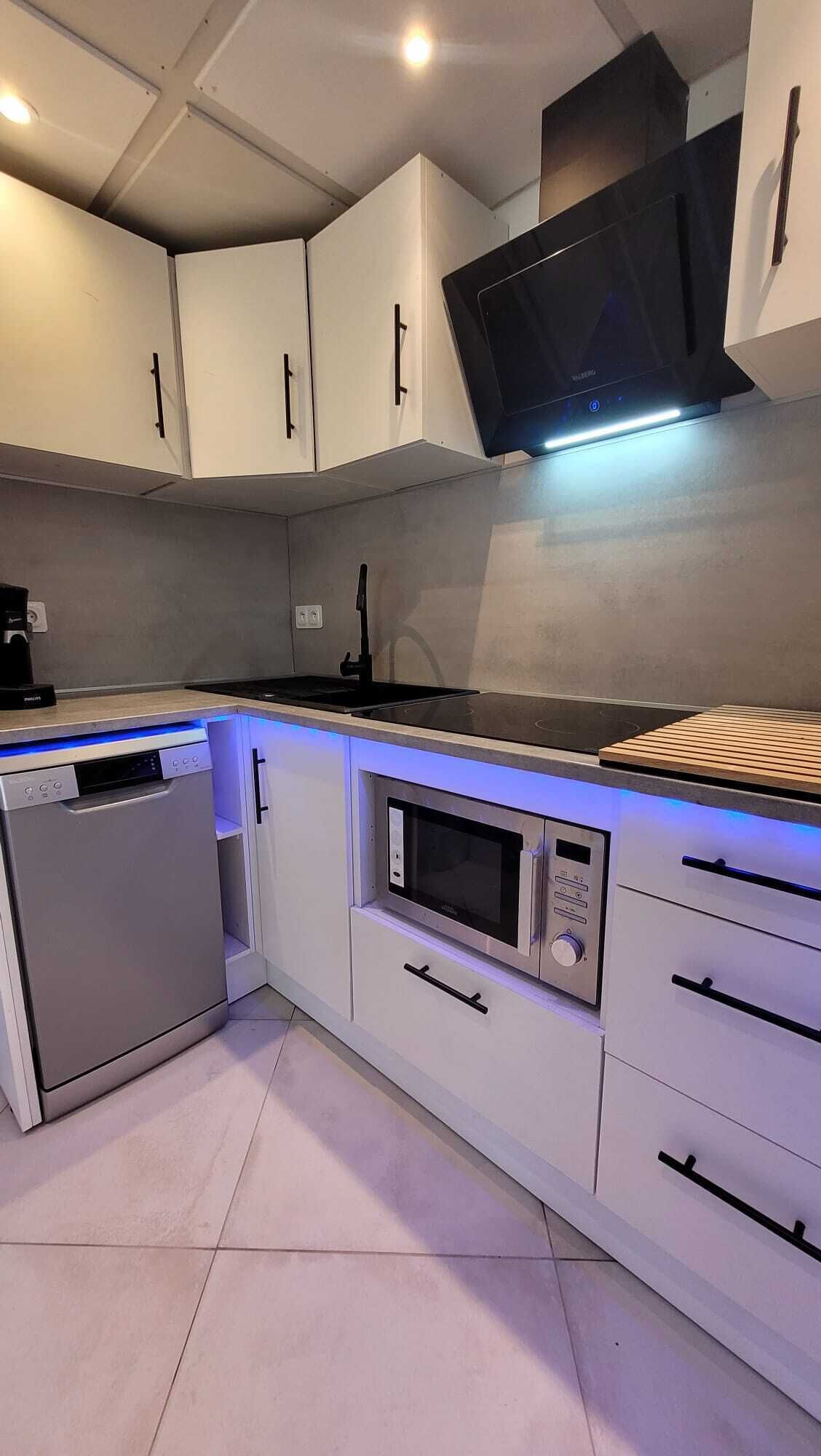 Une cuisine moderne avec des armoires blanches, un four à micro-ondes encastré, un lave-vaisselle et une hotte de cuisson noire.