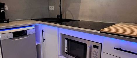 Une cuisine moderne avec des armoires blanches, un four à micro-ondes encastré, un lave-vaisselle et une hotte de cuisson noire.