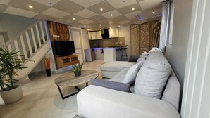 Un salon moderne avec un canapé, une table basse et un téléviseur. On y trouve un escalier avec une rampe et une plante.